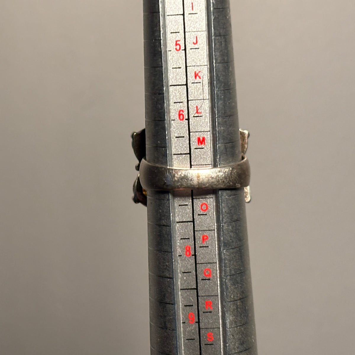A silver ring displayed on a metal ring sizer gauge showing its size, a size 7.