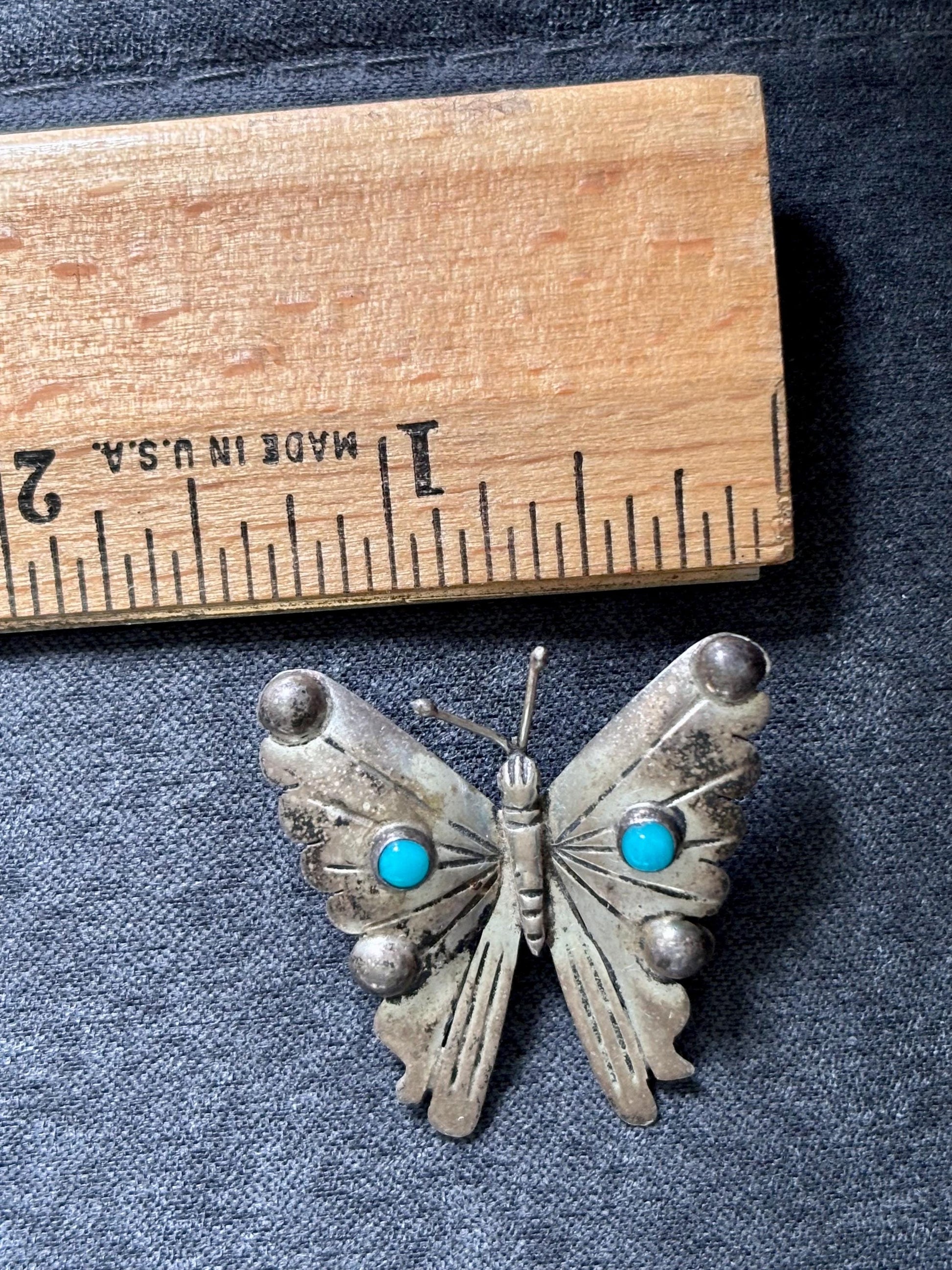 the brooch next to a ruler showing the dimensions of the top of the brooch from one wing to the other. it is approximately just under 1 1/2 inches