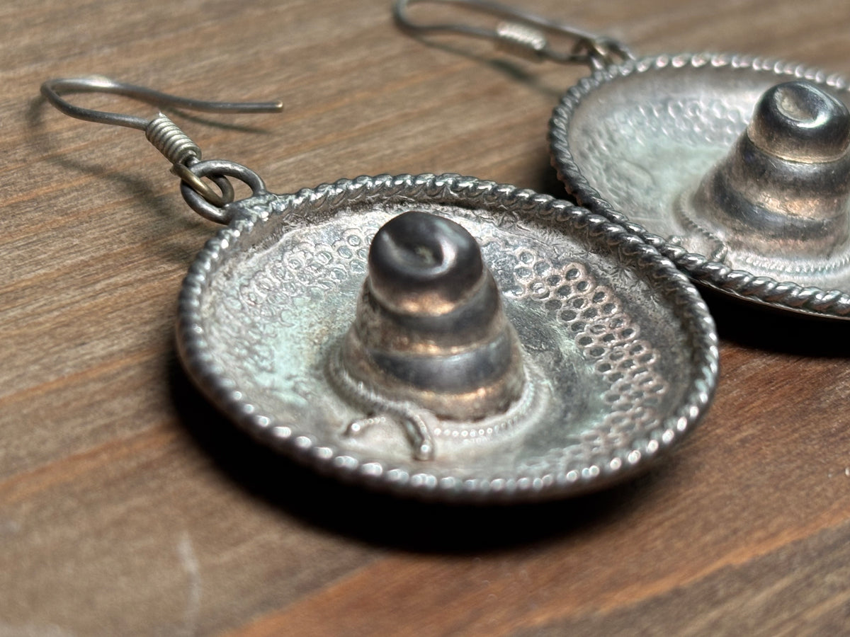 Close-up of sterling silver sombrero earring with textured brim, raised center, decorative rope edging, and oxidized finish.