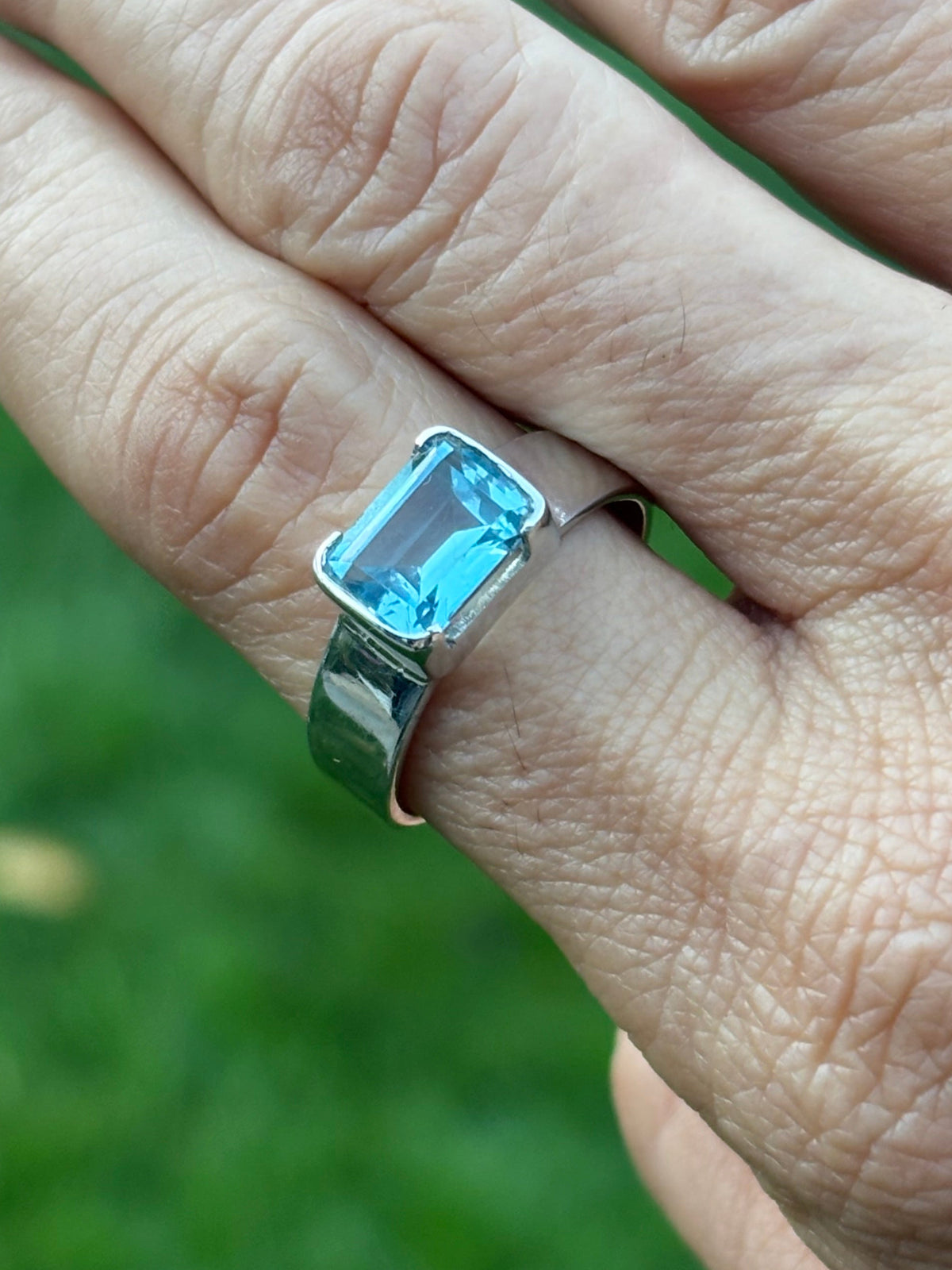 Sterling silver ring with a bright blue rectangular emerald-cut topaz in a polished silver setting, worn on a finger