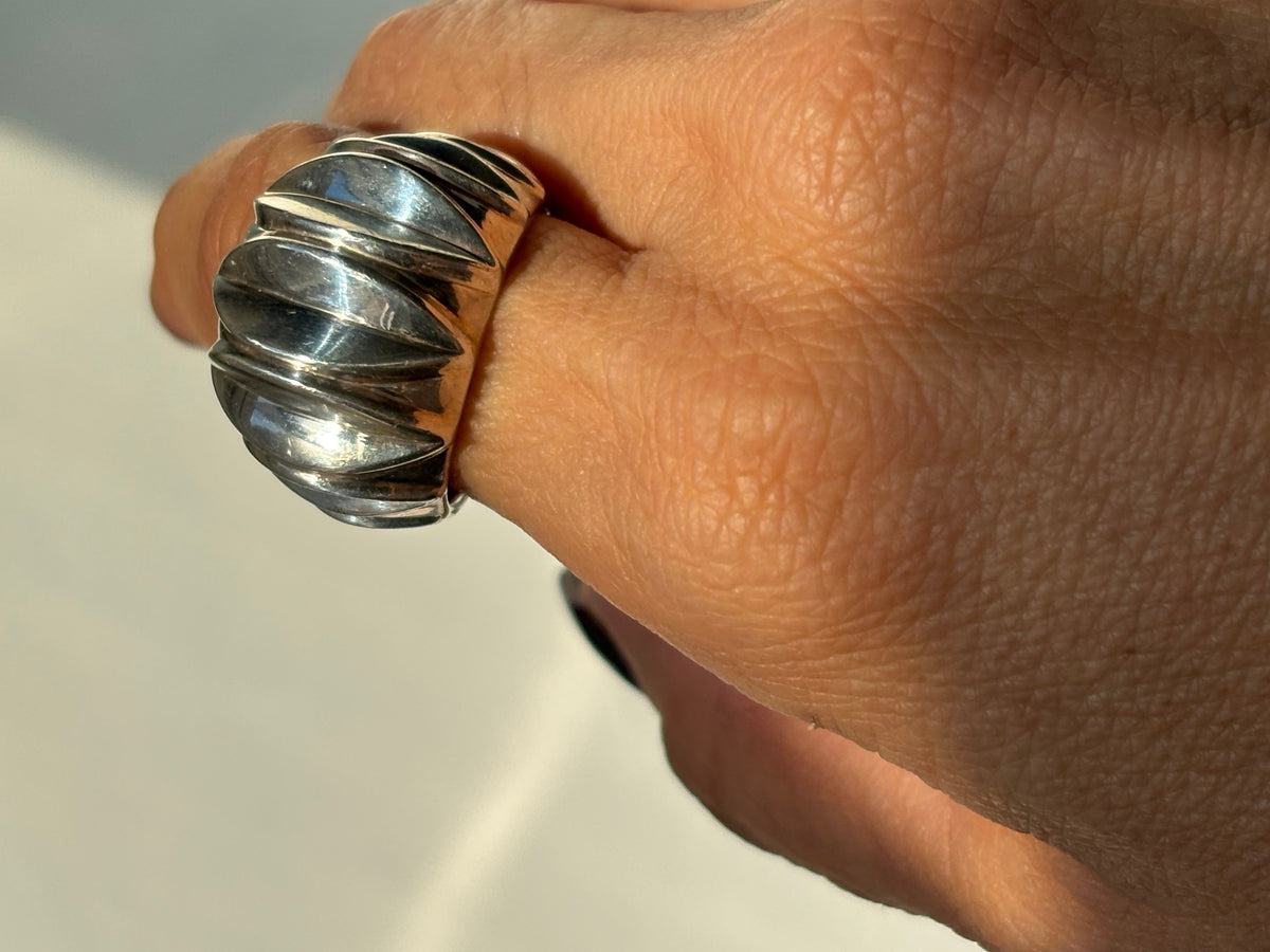 A close-up of a hand wearing a wide, chunky silver ring with a ribbed, textured design.