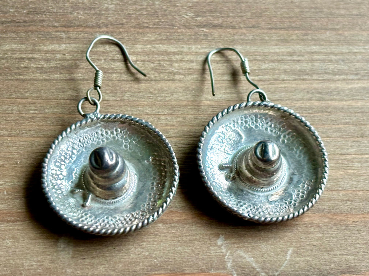 Pair of Mexican sterling silver dangling sombrero earrings with raised crowns, textured round brims, twisted rope borders, and French wire hooks.