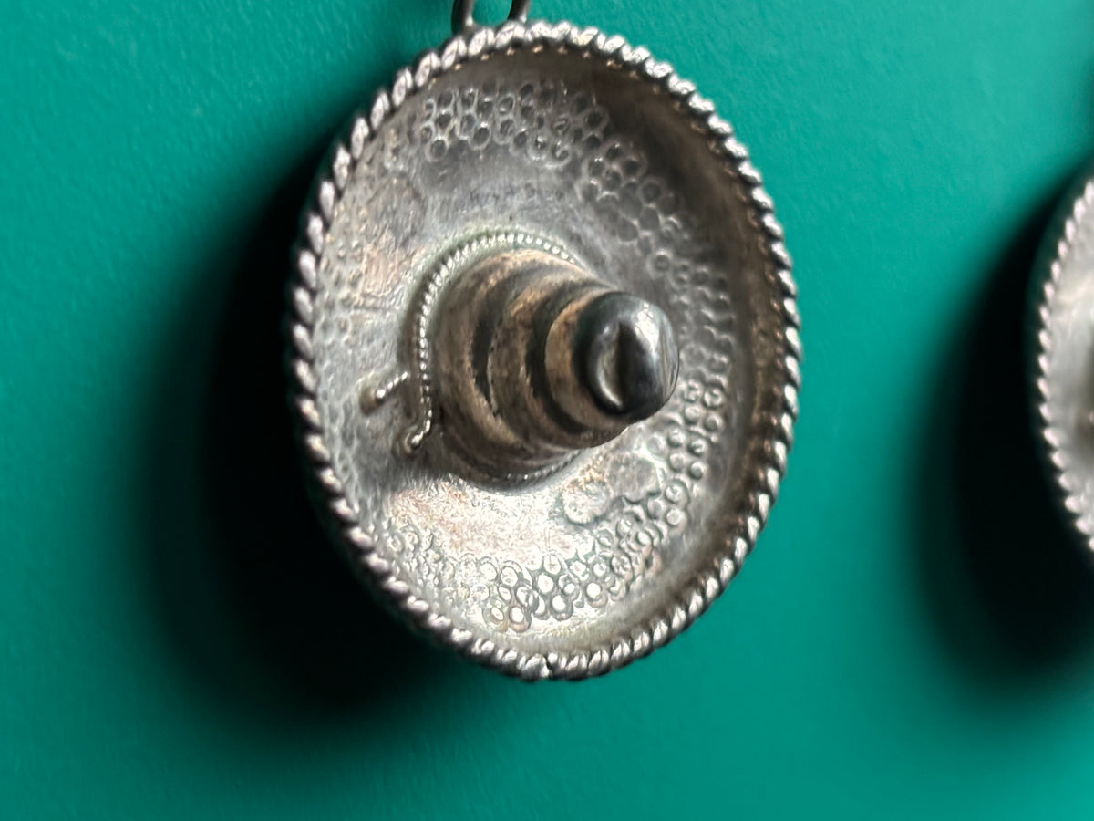 A close-up of the sombrero earring showing textured hammered surface, rope-style edge, and central protruding finial.
