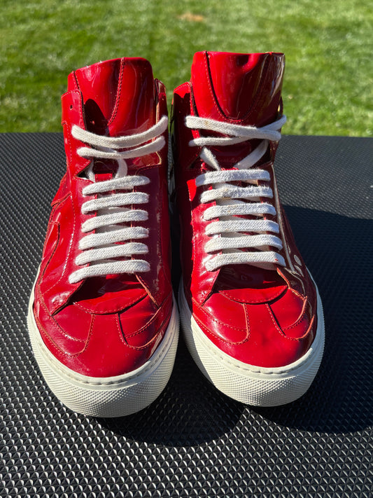 A pair of red patent leather high-top sneakers with white laces and white rubber soles