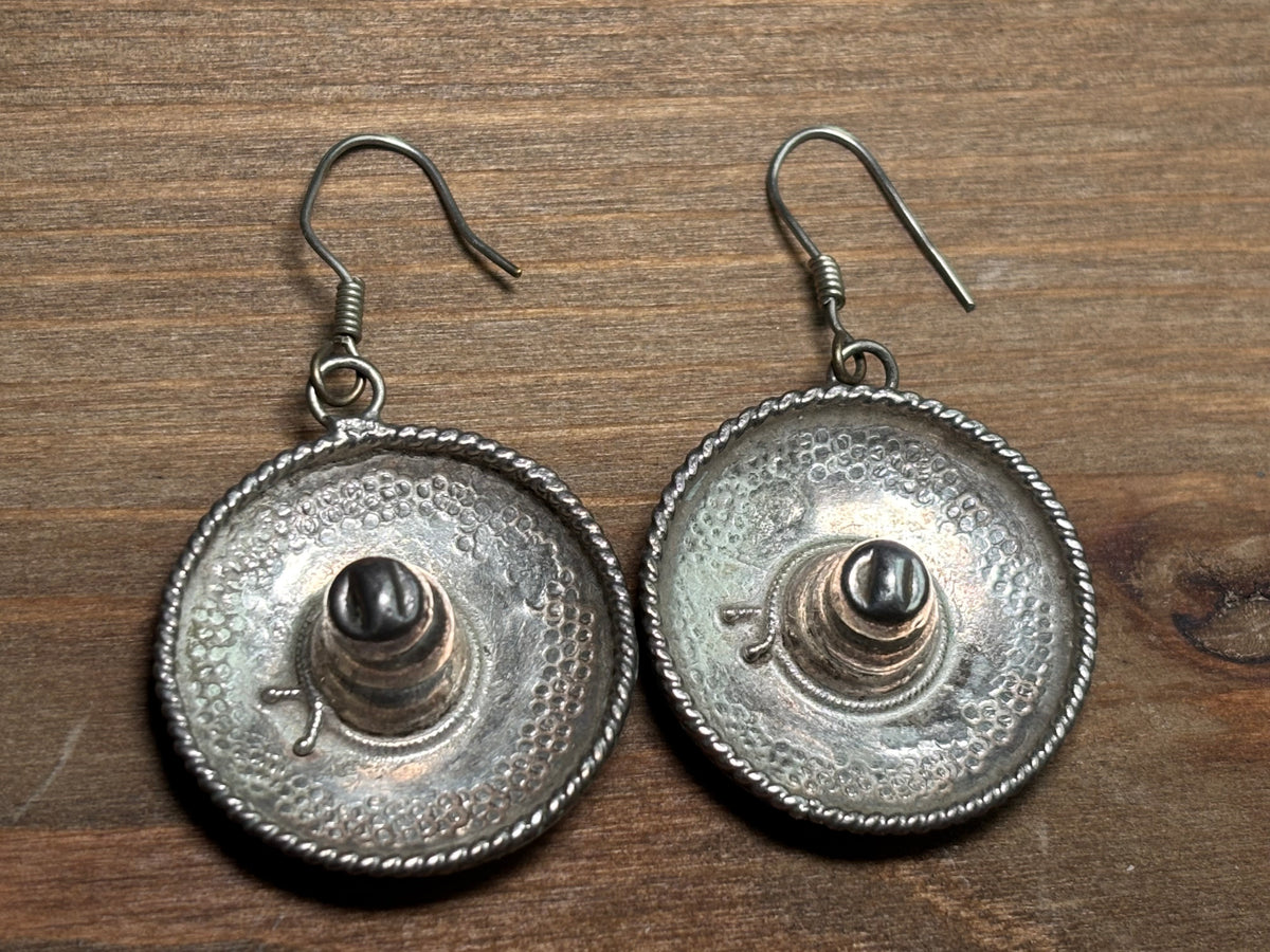 Pair of Mexican sterling silver dangling sombrero earrings with raised crowns, textured round brims, twisted rope borders, and French wire hooks.