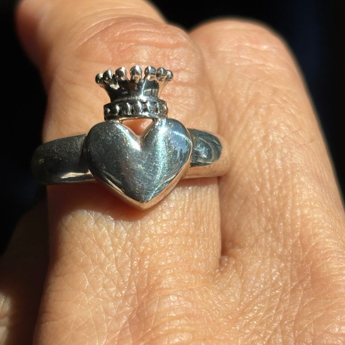 Silver crowned heart ring worn on finger, featuring a raised polished heart topped with a detailed silver crown with rounded points.