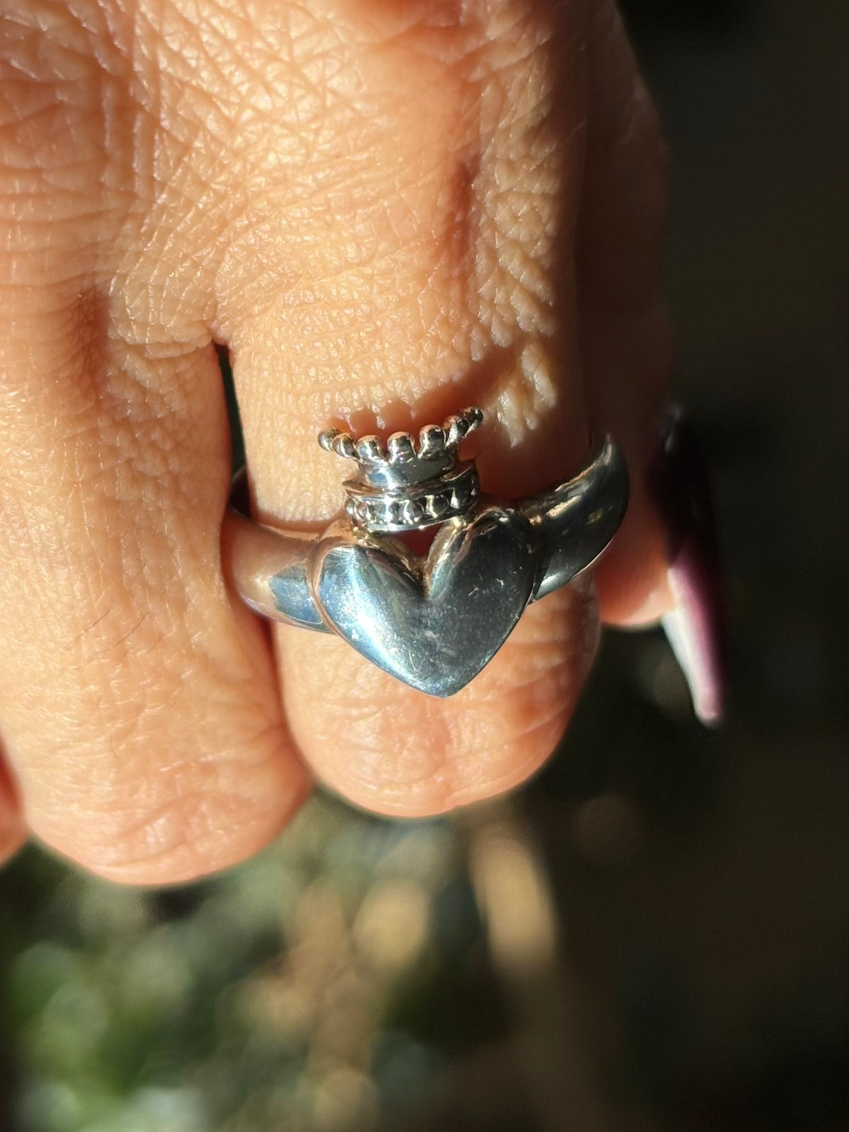 Silver crowned heart ring worn on finger, featuring a raised polished heart topped with a detailed silver crown with rounded points showing view from top of ring