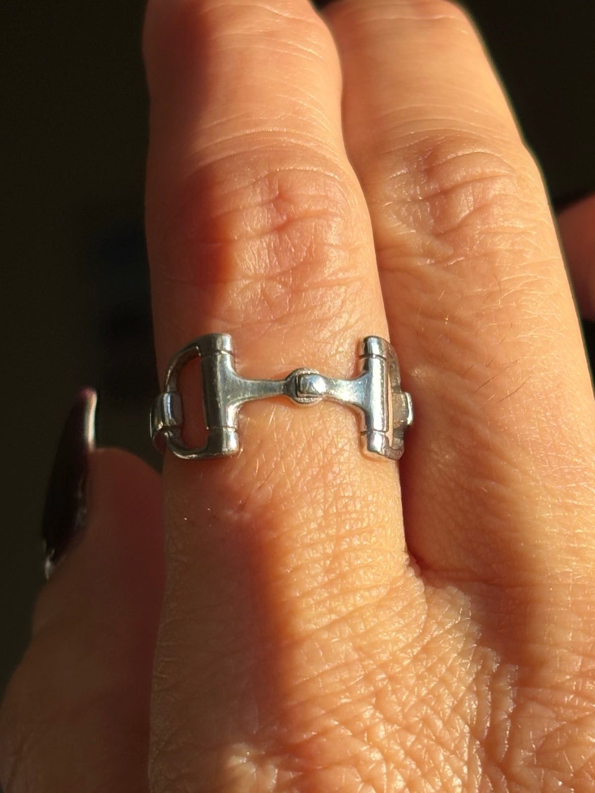 Sterling silver equestrian horsebit ring worn on finger, featuring an open snaffle bit design with polished silver ends and connecting center detail