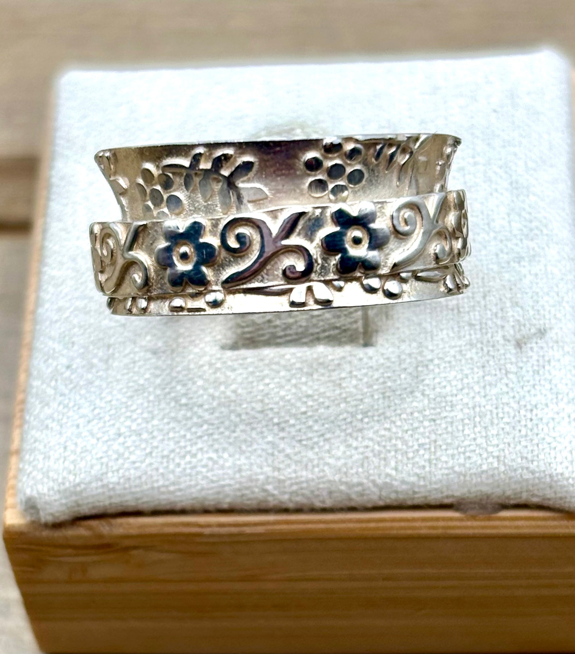 Silver ring with floral design on a white cushion 