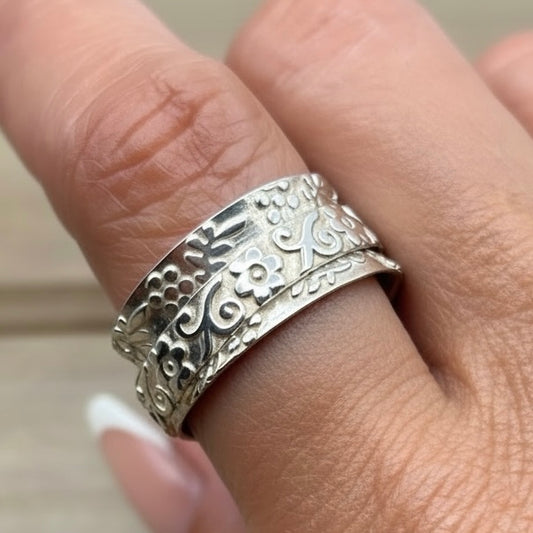 sterling silver spinner ring features an intricately engraved floral scroll design on a freely rotating center band. Decorative beaded edges frame the spinner.
