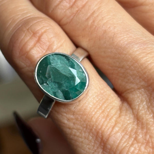 A close-up of a hand wearing a silver ring with a large, oval faceted green gemstone.